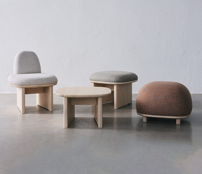 A set of modern furniture with a grey chair, two round ottomans—one grey, one orange—and a wooden coffee table on a concrete floor.