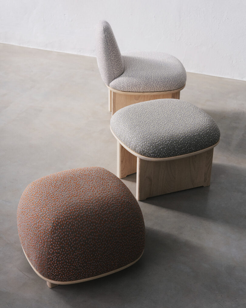 Three modern upholstered seats with wooden bases on a concrete floor, featuring neutral and muted color tones.