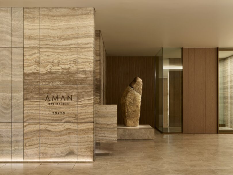 Lobby of Aman Residences in Tokyo with a large textured stone sculpture and modern interior design featuring stone and wood elements.