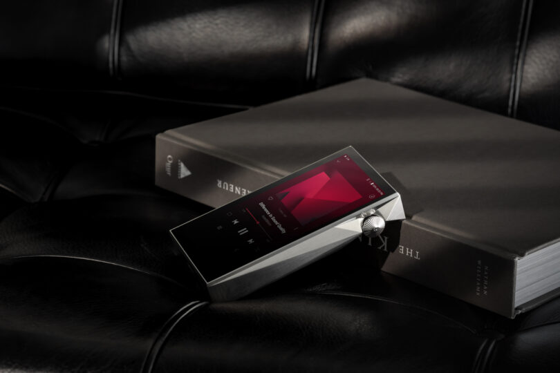 The SP3000M digital music player, featuring a sleek knob and playlist display, rests elegantly on a book atop the leather surface.