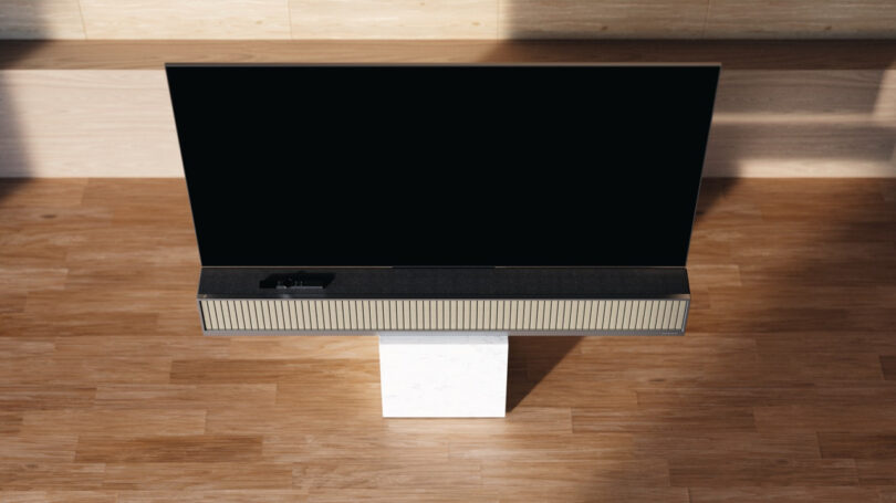 Flat screen TV with a black screen sits elegantly on a white stand, its sleek design complemented by Dynaudio speakers, all resting on a warm wooden floor.