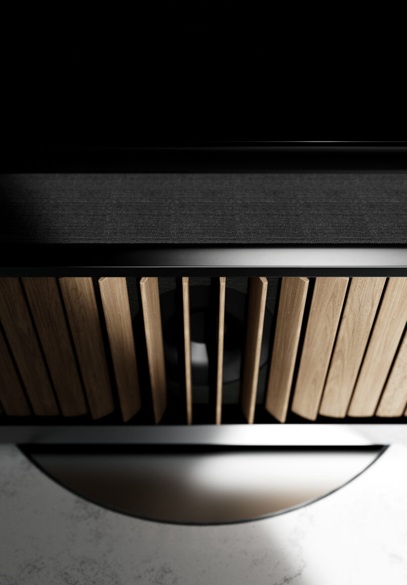 Close-up view of a modern Dynaudio speaker with vertical wooden slats, a black mesh grille, and a circular metallic base on a light surface.