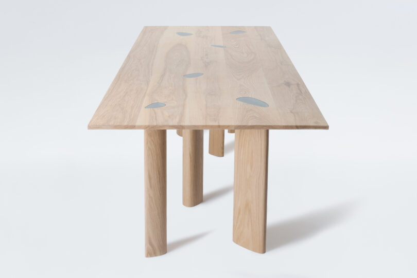 A wooden table with a rectangular top and cylindrical legs, featuring abstract gray inlays on the surface