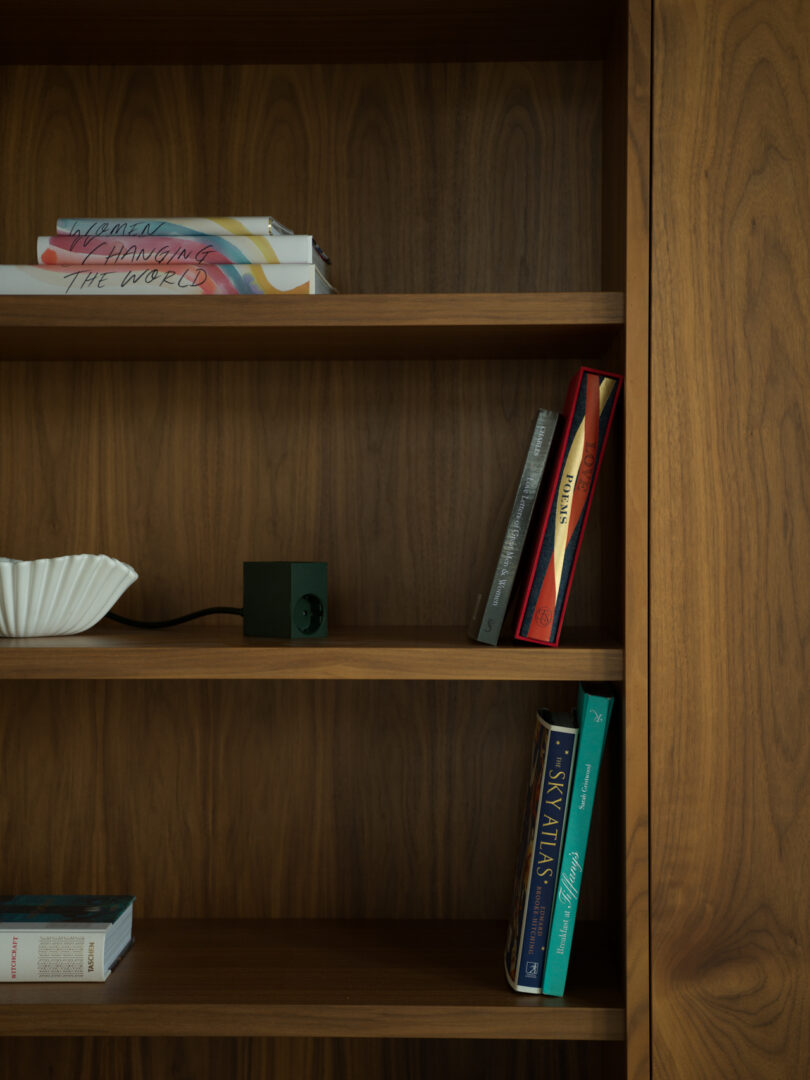 A wooden bookshelf holds a few scattered books and a Kord object on the middle shelf. To the left, a white decorative bowl adds a touch of elegance.