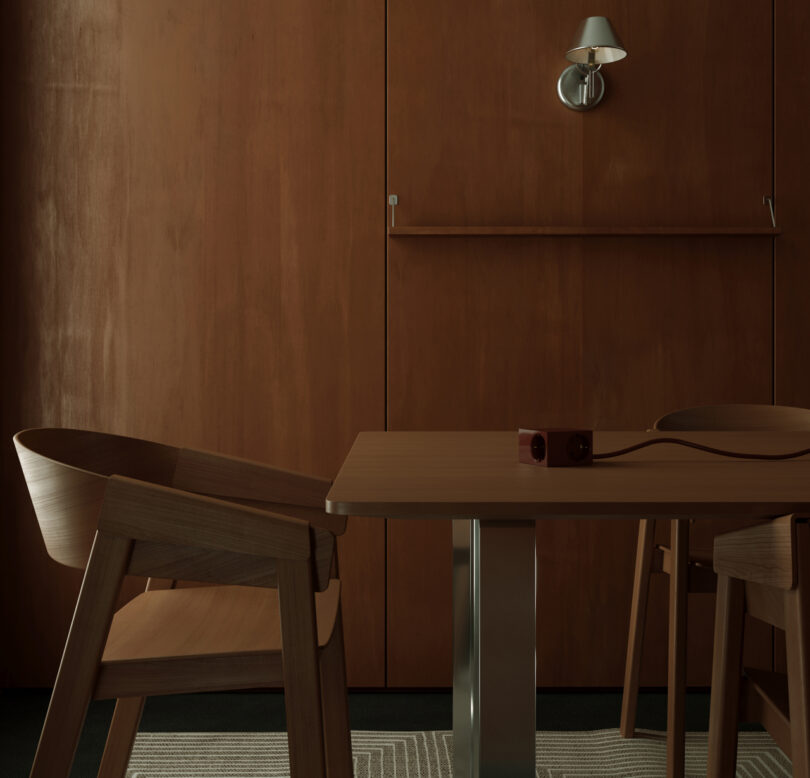 A minimalist dining area features wooden chairs and a table against a dark kord wood wall. Above the table, a wall-mounted light and small shelf add functionality.