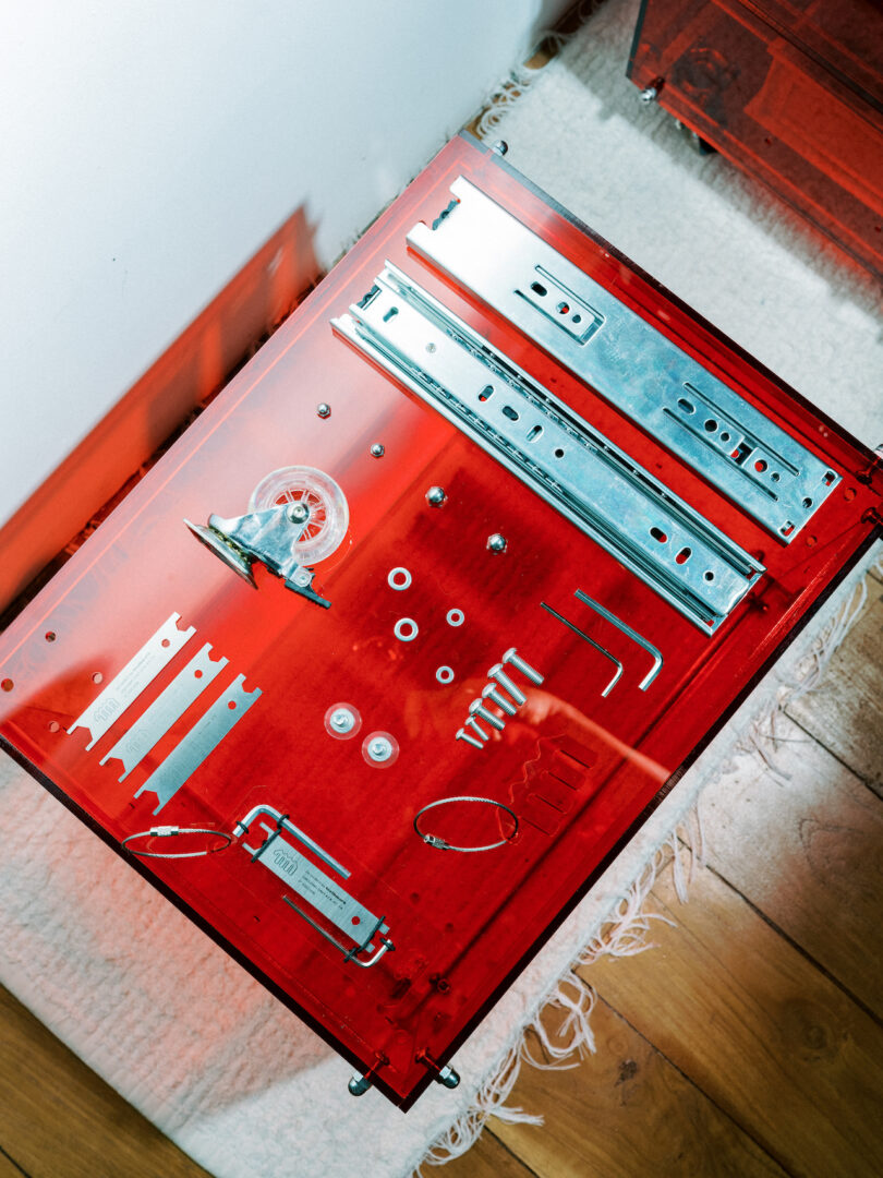 Red table with assorted metal tools and parts, including screws, brackets, and an allen wrench, arranged neatly on top