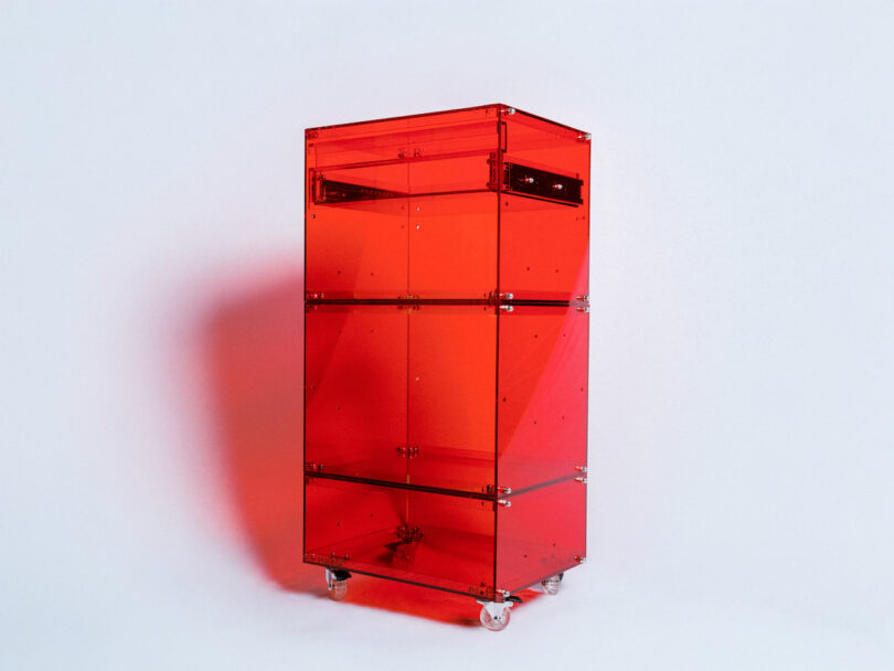 A red transparent standing cabinet on wheels with metal hinges and screws, placed against a white background