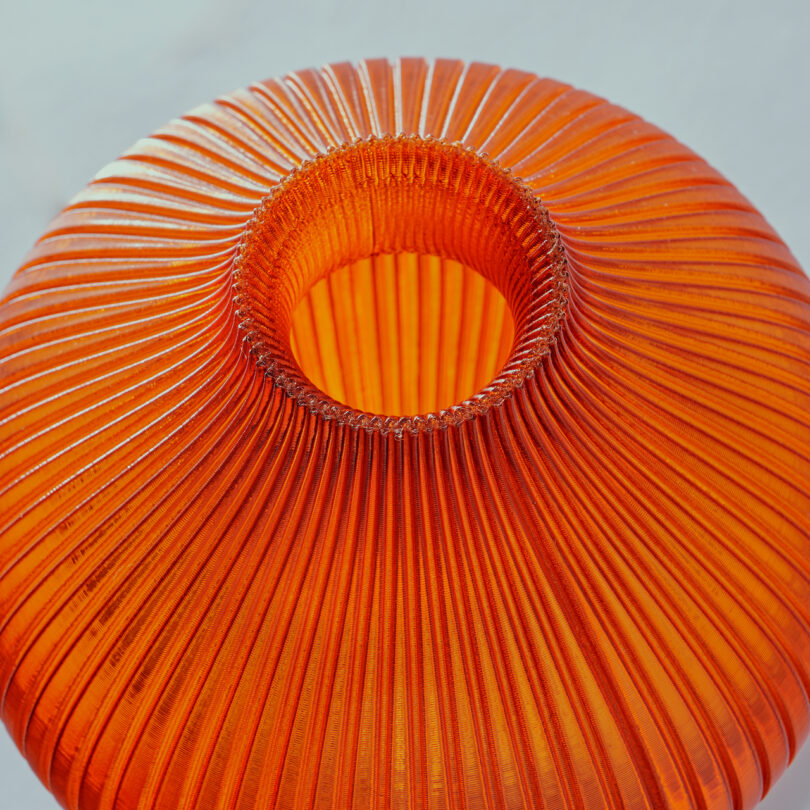 Close-up of a round, orange fluted vase with vertical ridges, viewed from above