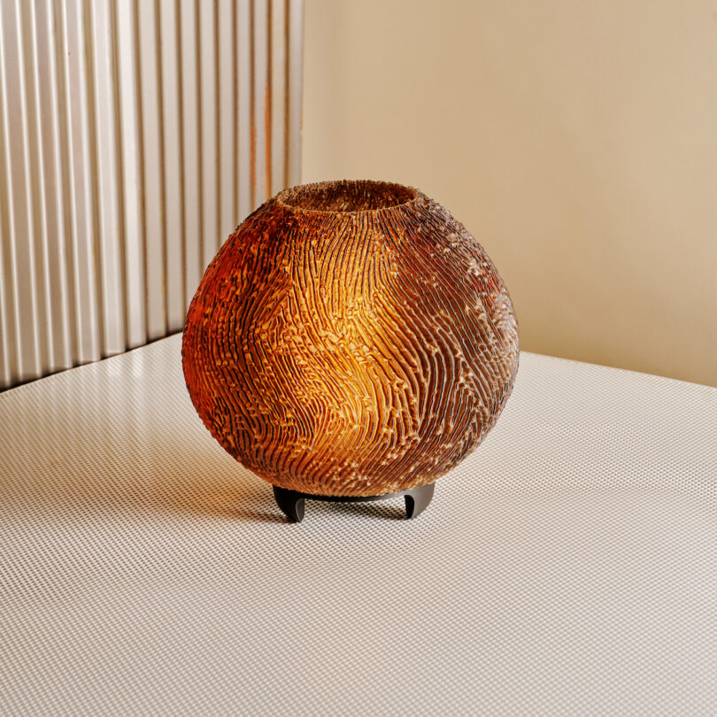 A textured, spherical lamp with a warm glow sits on a white, textured surface against a ribbed wall