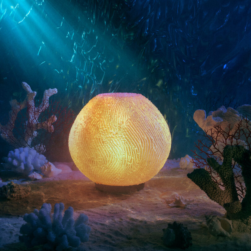 A glowing spherical lamp on the ocean floor, surrounded by coral and illuminated by rays of light from above.