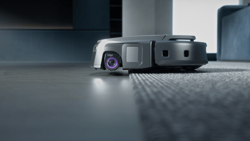 A robotic vacuum cleaner is moving from a hard floor to a carpeted area, captured at floor level.