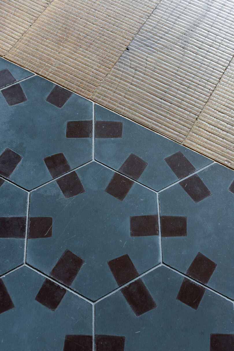 Geometric floor tiles with a pattern of dark rectangles on a blue hexagonal background meet diagonally with beige rectangular tiles.