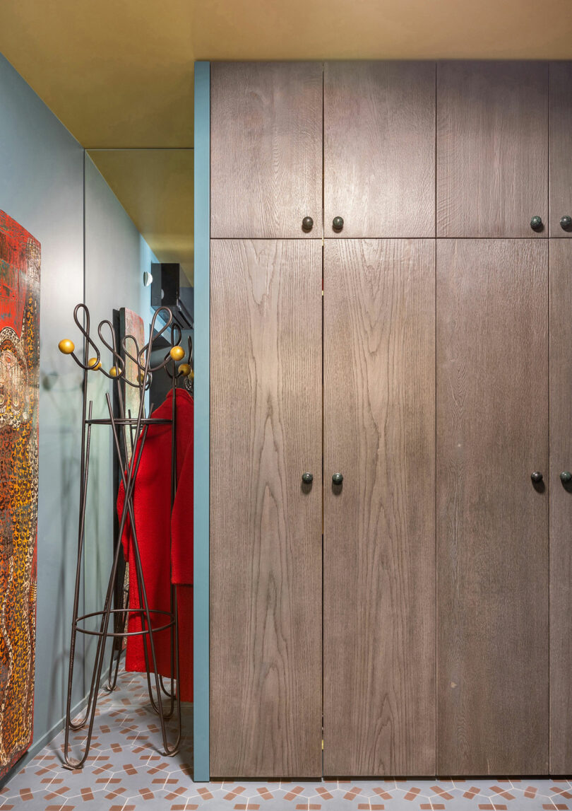 A hallway with wooden cabinets, a colorful coat rack with jackets, and a patterned floor.