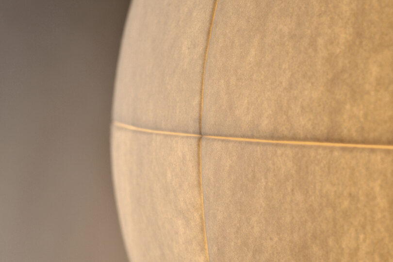 Close-up of a spherical lamp with a textured surface, intersected by visible seams creating four distinct segments. The warm light and soft focus create a blurred background.