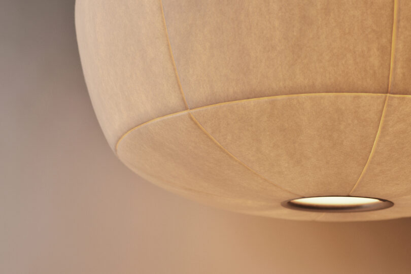A close-up of a beige fabric lampshade with visible stitching and a circular light source at the bottom.