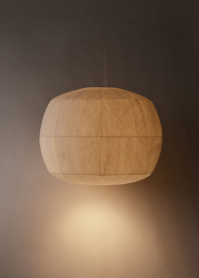 A spherical, beige hanging lamp emits a warm, soft glow against a neutral background.