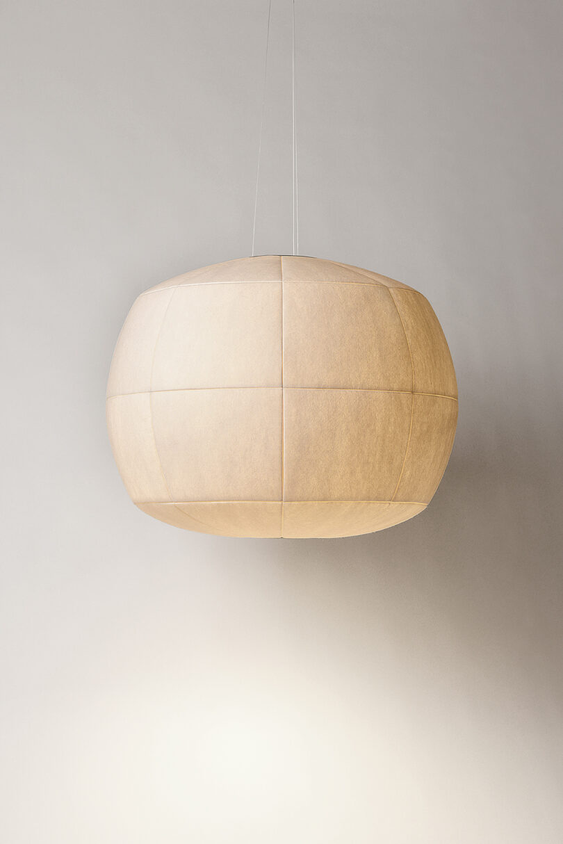 A round, beige pendant light fixture hangs from the ceiling against a plain gray background.