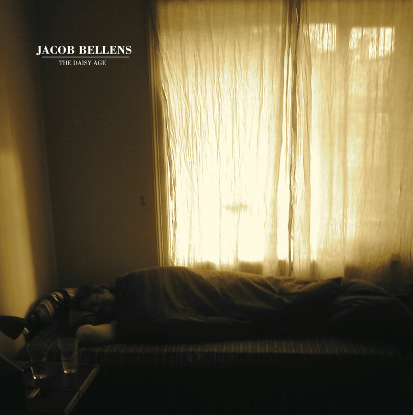 A person sleeps on a bed against a window with sheer curtains, creating a soft glow in the room. Two glasses are placed on a table nearby. Text reads, "Jacob Bellens: The Daisy Age," with artistic direction by Stine Find Osther.