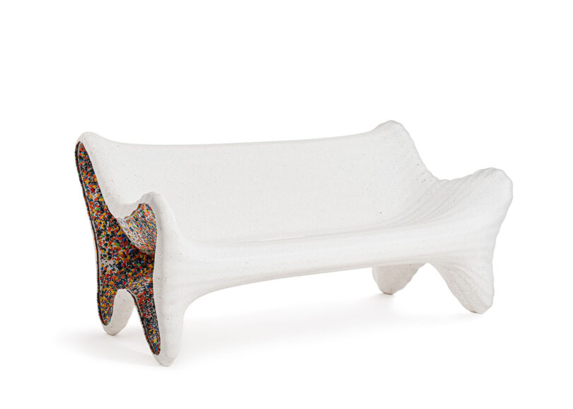 A modern white sculptural bench with curved edges and colorful speckled detailing on the inner sides, inspired by the In-Side Thomas Heatherwick approach to innovative design.