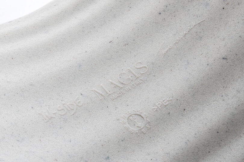 Close-up of embossed branding and text on a light gray textured surface, featuring "MAGIS MADE IN ITALY," In-Side Thomas Heatherwick, and other markings.