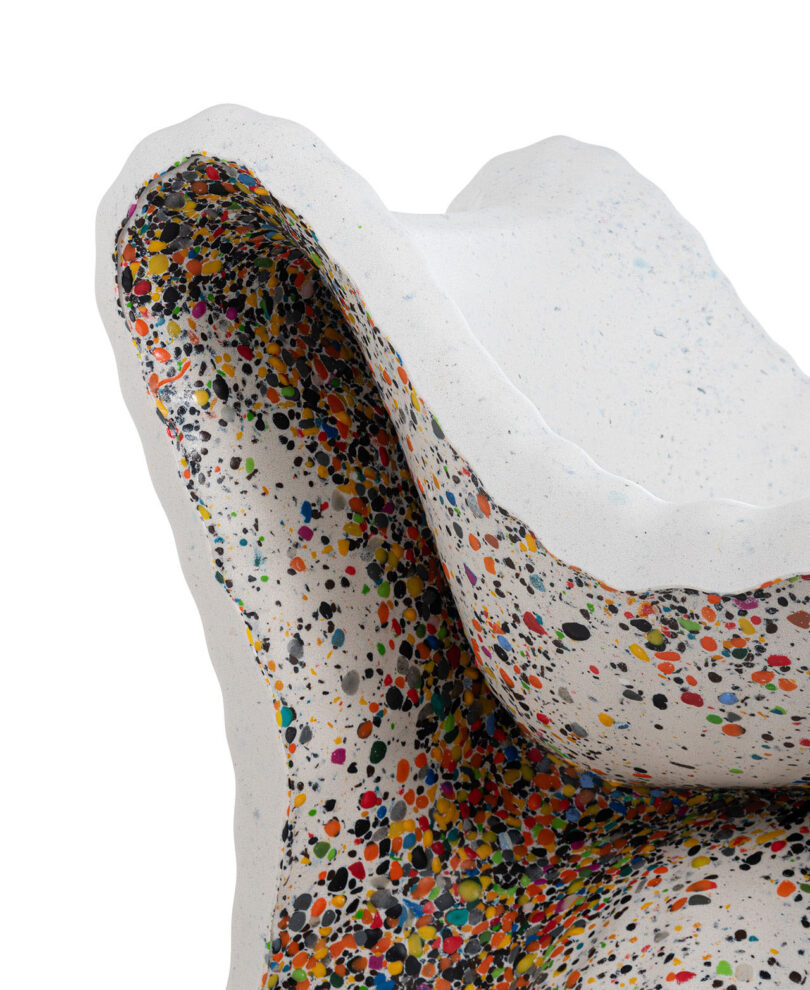 Close-up of a sculpted white object from In-Side Thomas Heatherwick, with an irregular shape and colorful paint splatters concentrated on the inner surface.