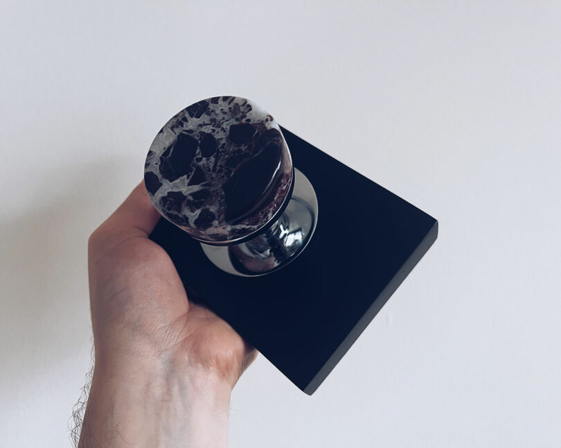 A hand holds a black block with a round marble handle, reminiscent of the sophisticated designs showcased at KBIS, against a plain white background.