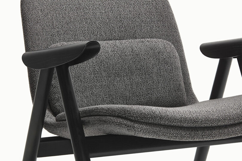 Close-up of a modern Keilhauer chair with dark wooden armrests and legs. The upholstery showcases a textured gray fabric, complemented by a cushioned backrest.