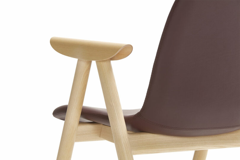 Close-up of a modern chair by Keilhauer, featuring a wooden armrest and legs, with a sleek brown leather backrest and seat.