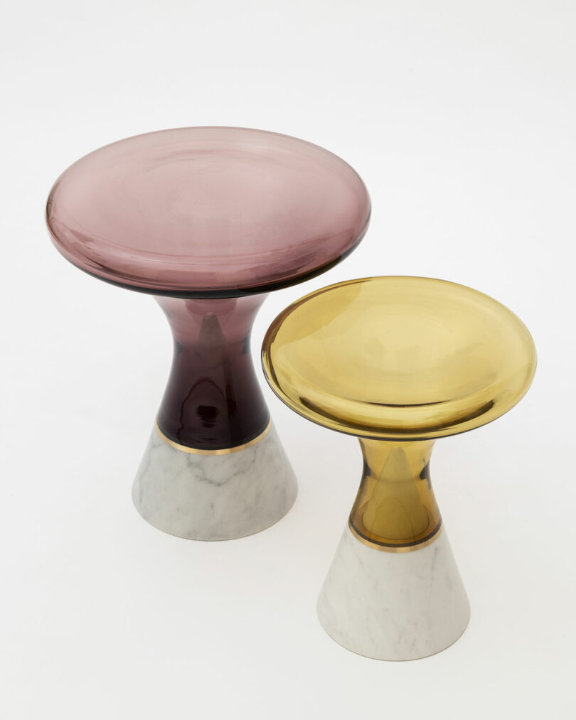 Two pedestal tables with marble bases and glass tops join form and function in your living space; one features a pink top while the other dazzles with a yellow top, making them perfect pieces for any field of design.