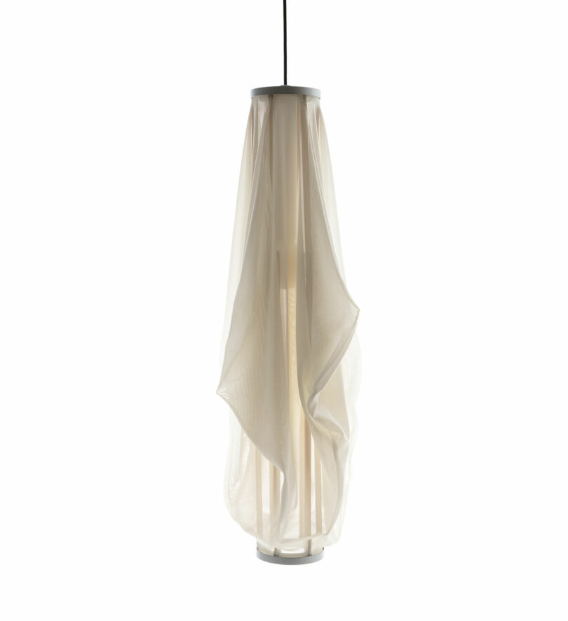 The Sorpresa pendant light, designed by Samuel Wilkinson, features a modern cylindrical fabric shade that is slightly translucent and elegantly suspended from a black cord.