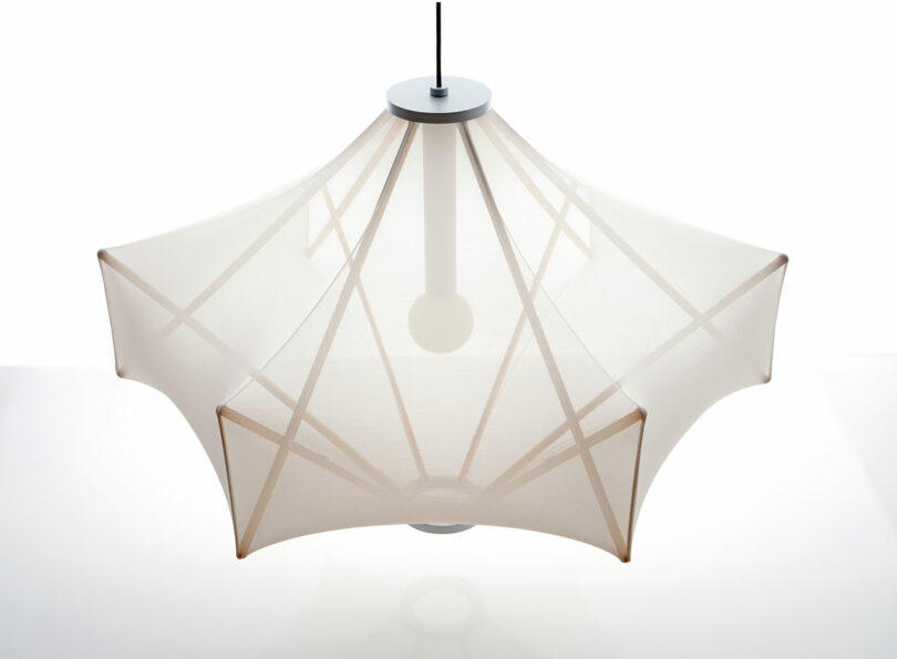 A modern pendant lamp designed by Samuel Wilkinson features a star-shaped fabric shade and showcases a central bulb. Hanging from the ceiling, the Sorpresa design boasts angular lines and a translucent appearance.