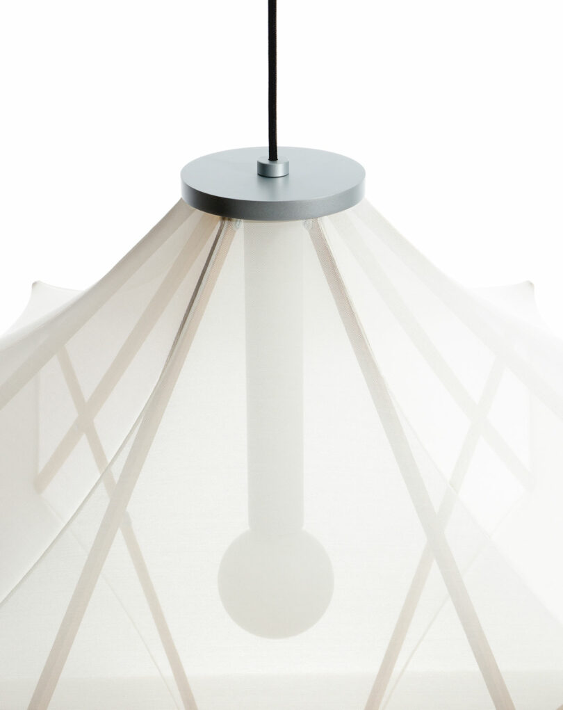 Close-up of the Sorpresa pendant light by Samuel Wilkinson, featuring a modern design with a white fabric shade, black cord, and visible bulb inside.