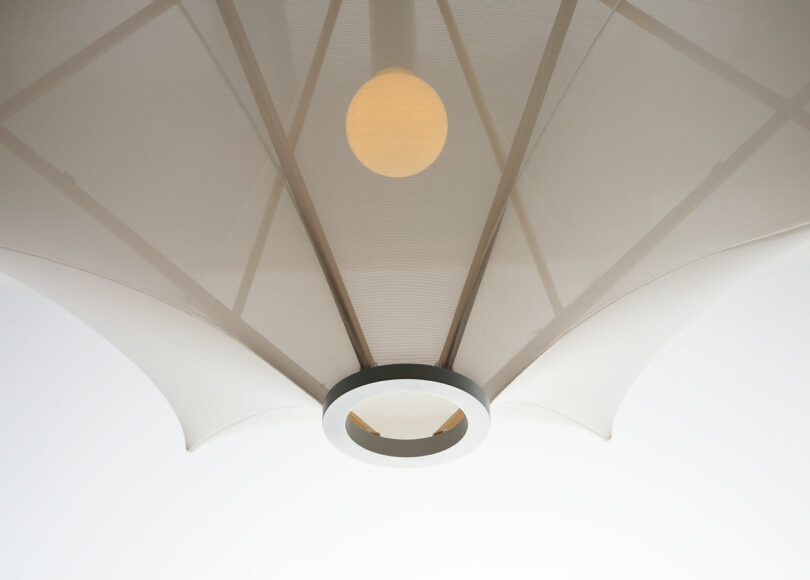 This ceiling-mounted light fixture, a Sorpresa designed by Samuel Wilkinson, features a round bulb encased in a geometric, translucent shade resembling an umbrella.