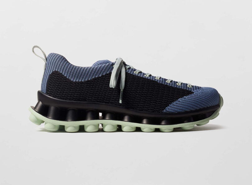 Blue and black knit sneaker with a light green sole and laces, featuring a textured pattern and a modern design.