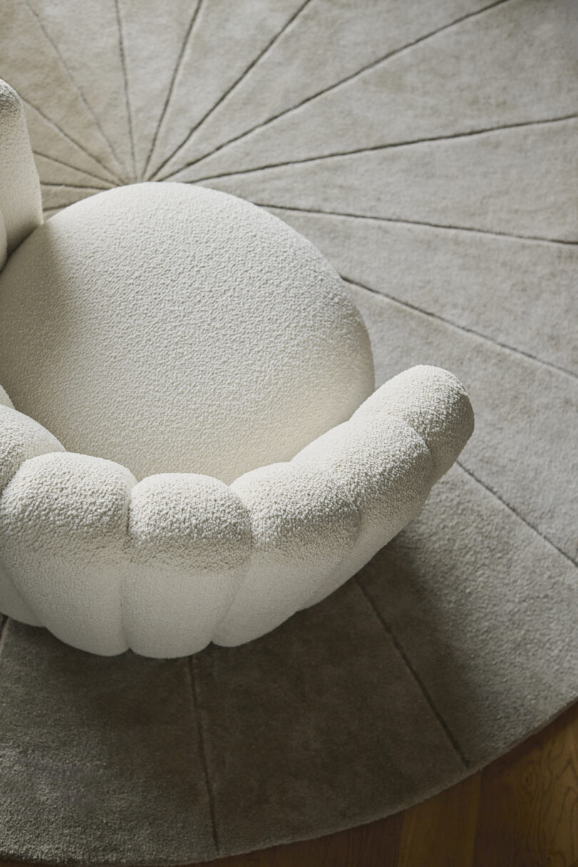 A textured, white upholstered chair sits on a circular, gray rug with a radial pattern.