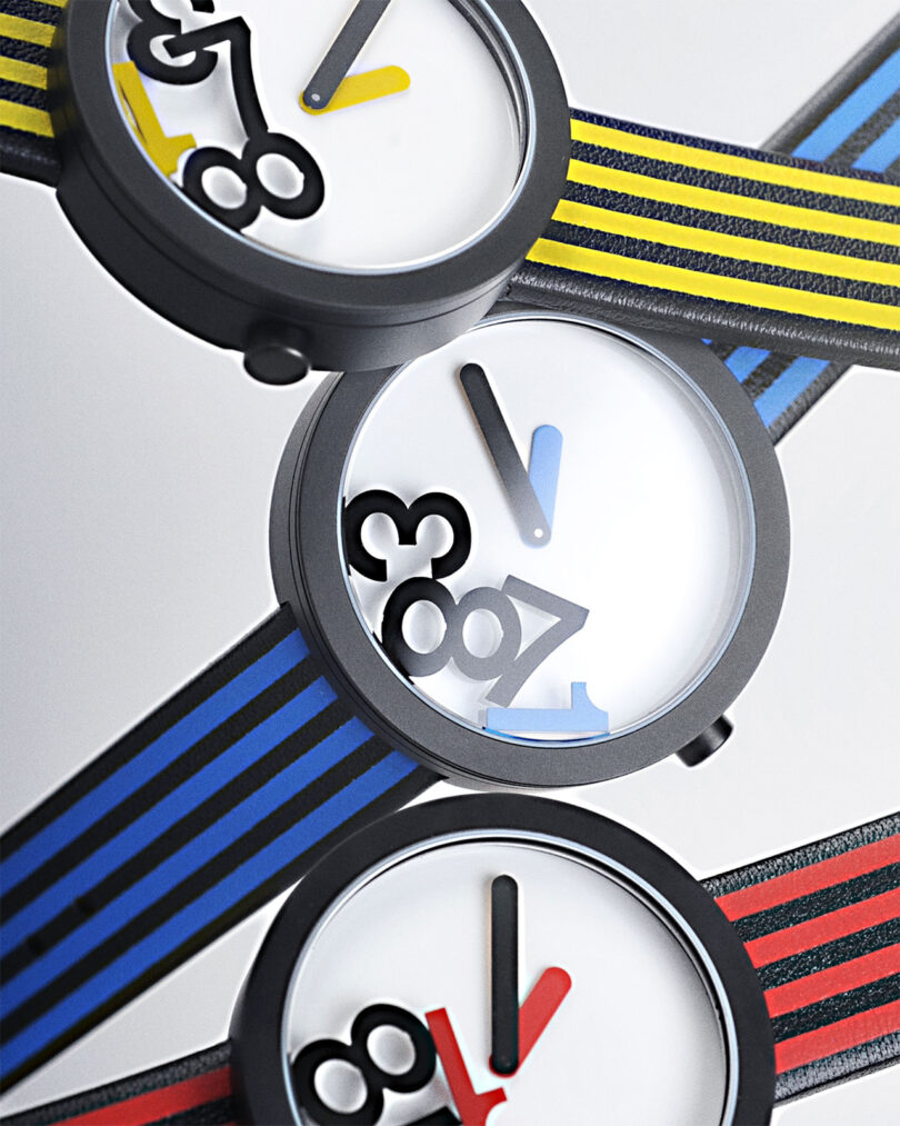 Three watches with striped bands in blue, yellow, and red are positioned diagonally. Each watch has a white face with black numerals and unique hand colors matching their respective bands.