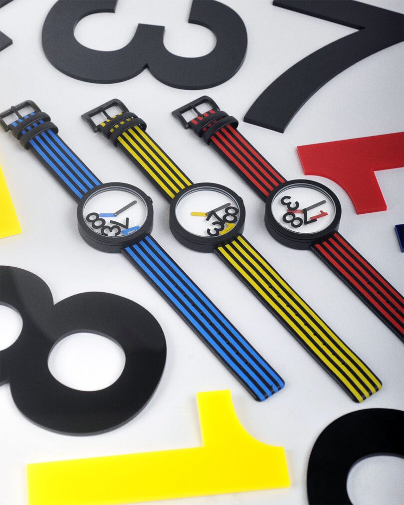 Three colorful wristwatches with striped bands are arranged on a surface scattered with large black and red numbers.