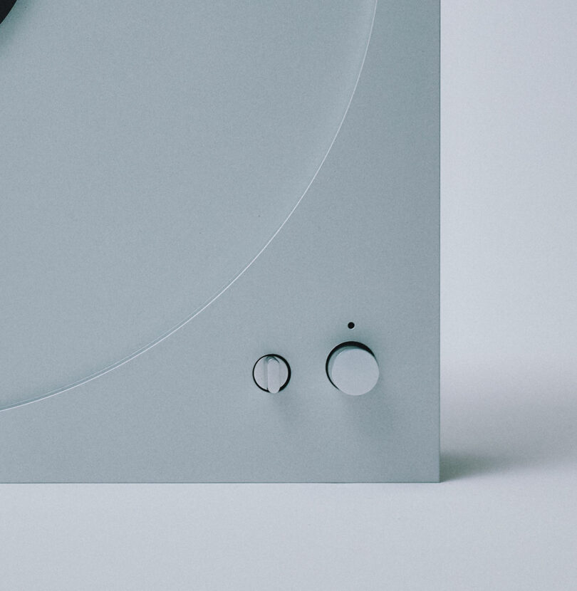 Close-up of a minimalistic gray turntable, model PP-1, featuring two sleek knobs on the bottom right.