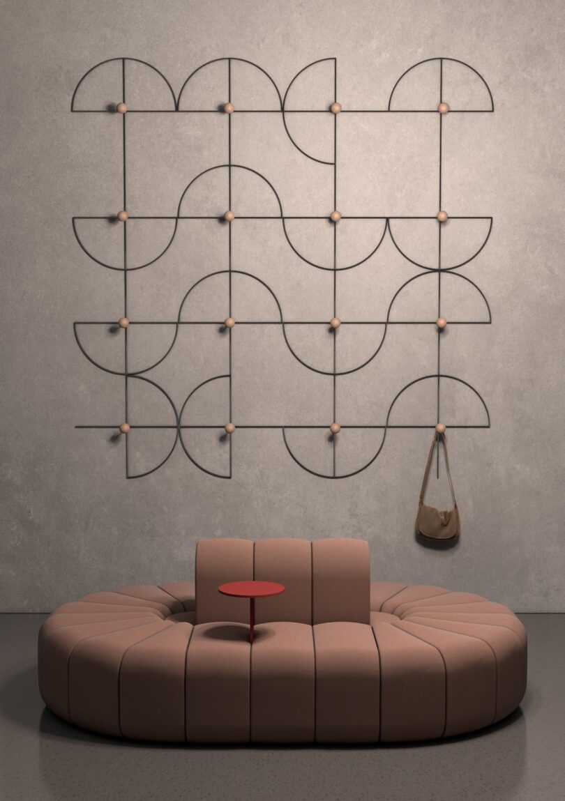 Circular beige sofa with a red table in the center. Geometric wall art and a hanging brown bag adorn the gray wall behind
