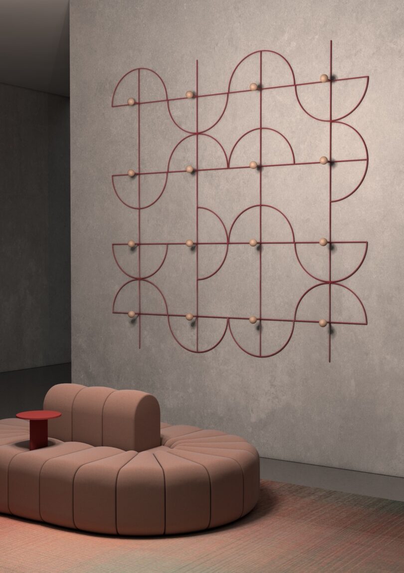 Modern room with a curved, modular brown sofa and a geometric wall sculpture featuring intersecting red lines and circular nodes. The floor is a muted shade, complementing the neutral color scheme