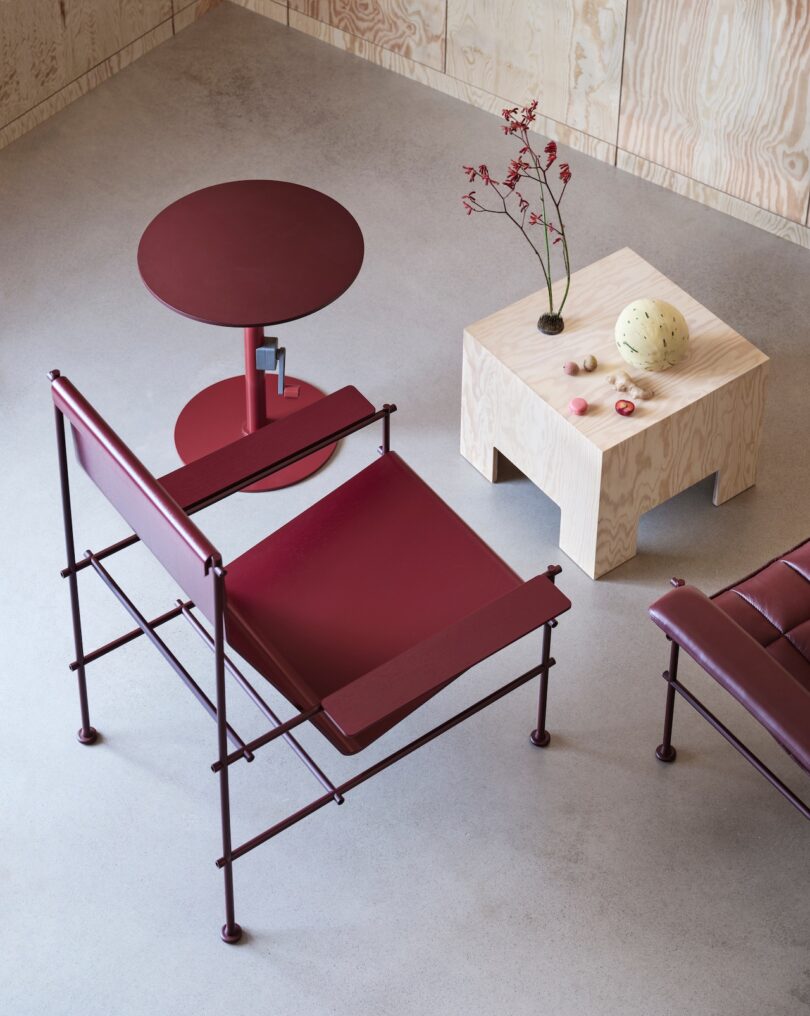 Modern minimalist room with a red chair, round red table, square wooden table with a vase and fruit, on a gray floor