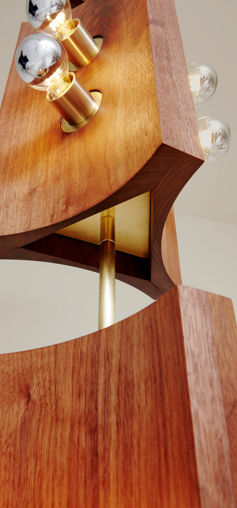 Close-up of a modern wooden light fixture by Blue Green Works, featuring elegant brass accents and three visible light bulbs illuminating from the top.