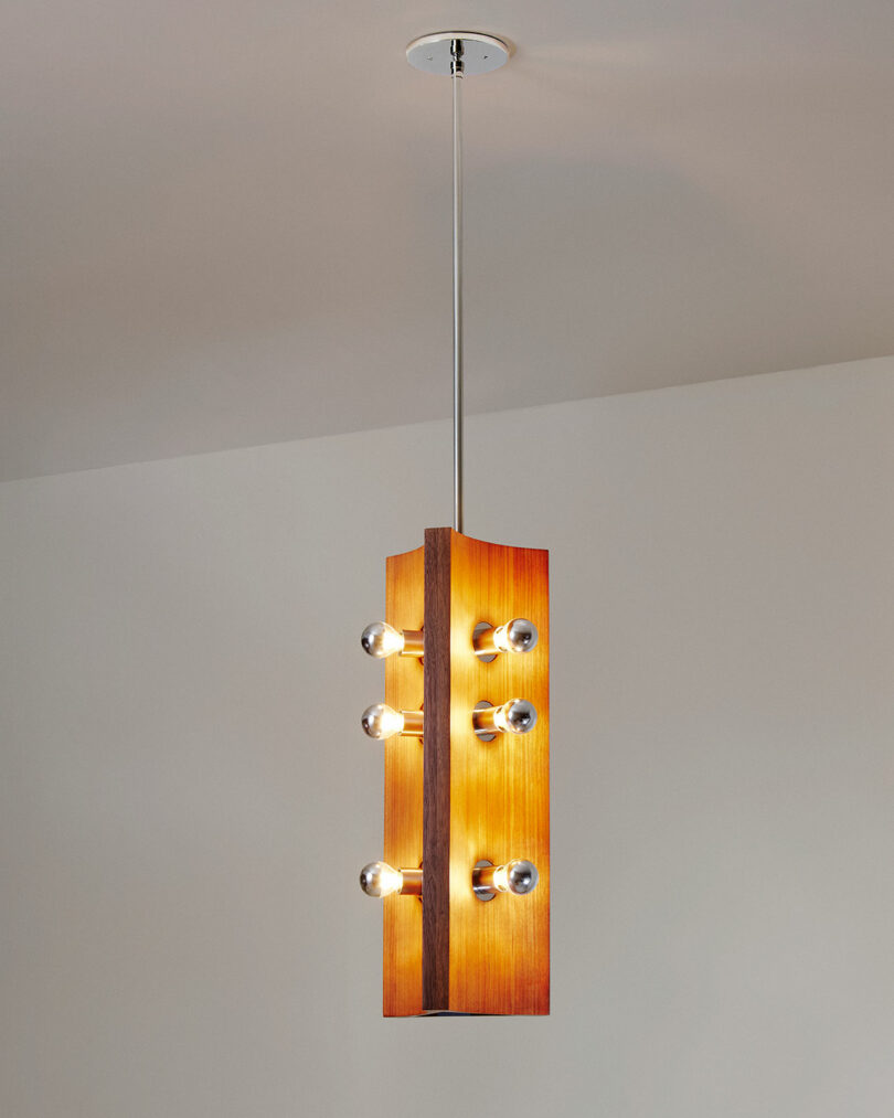 Wooden pendant light fixture by Blue Green Works, featuring exposed bulbs in a vertical arrangement, hanging elegantly from the ceiling against a neutral wall.