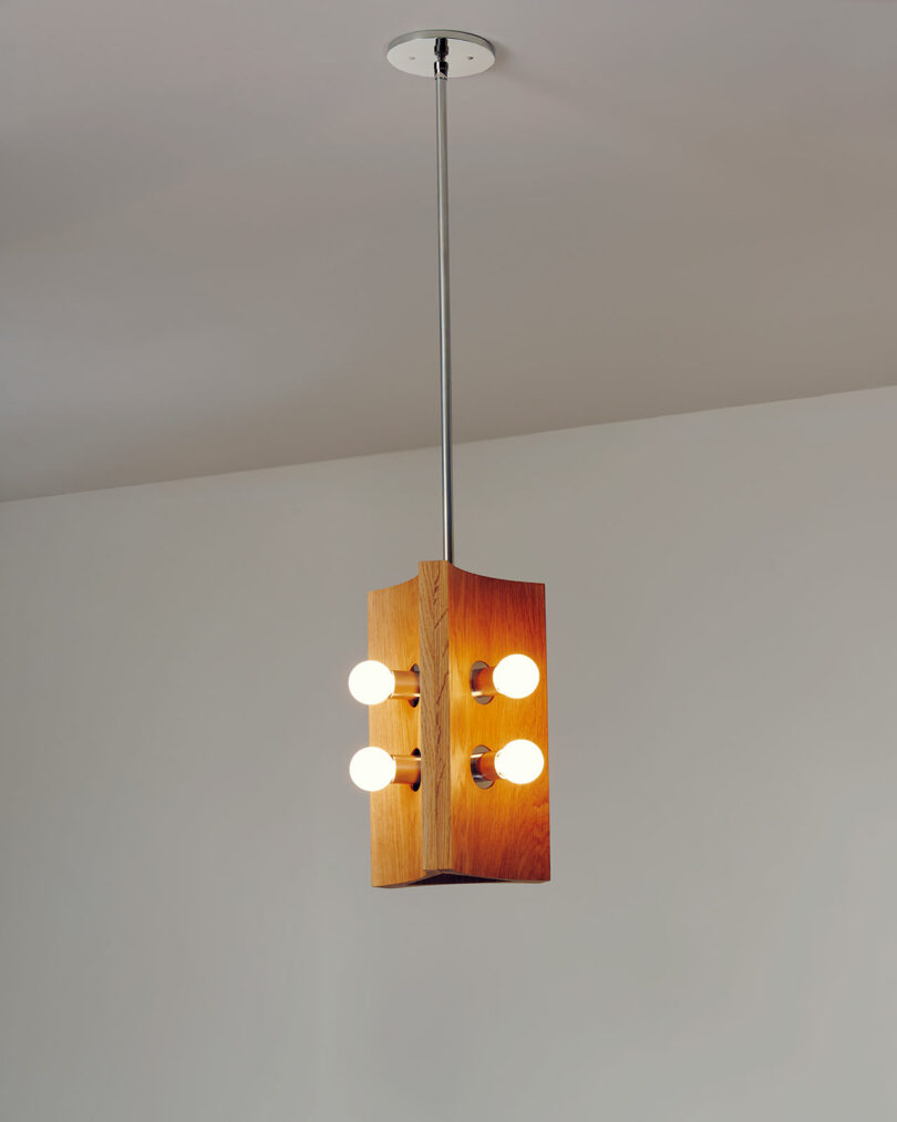 A pendant light fixture with a wooden rectangular frame, crafted by Blue Green Works, hangs from the ceiling and features four exposed light bulbs.