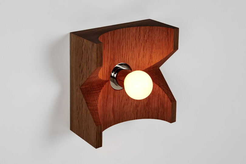 This Wooden wall-mounted light fixture by Blue Green Works features a glowing bulb elegantly nestled in a central circular groove.