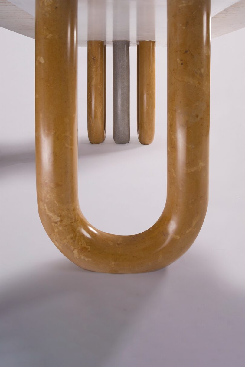 Close-up of the underside of a table with U-shaped legs in beige and one gray in the background on a white surface