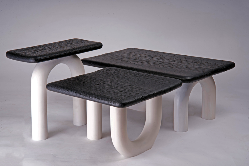 Three modern tables with textured black tops and curved white legs, varying in height, arranged together on a neutral background
