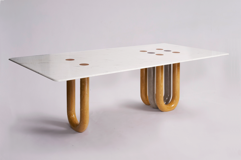 A modern rectangular table with a white marble top featuring circular inlays and uniquely curved wooden legs on a plain background
