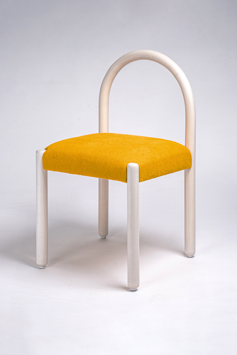 A chair with a white arched backrest, white cylindrical legs, and a yellow cushioned seat on a gray background