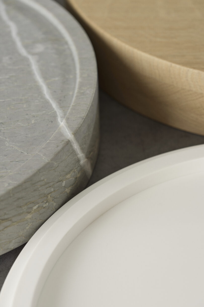 Close-up of three overlapping circular objects with different textures: a gray marble surface, a light wood surface, and a smooth white surface, arranged on a flat, dark background